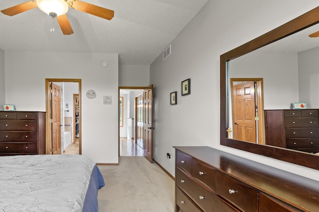 bedroom featuring ceiling fan, a textured ceiling, ensuite bathroom, and light carpet