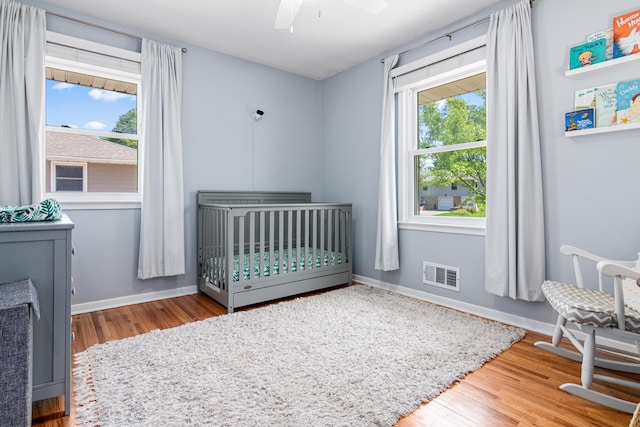 bedroom with wood finished floors, a crib, baseboards, and ceiling fan