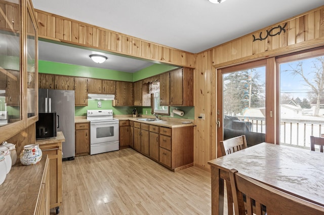 kitchen featuring light wood-type flooring, white electric range, sink, wood walls, and stainless steel refrigerator