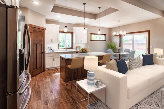 kitchen with pendant lighting, stainless steel fridge, a raised ceiling, white cabinets, and a center island