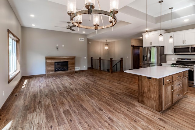 kitchen featuring a center island, white cabinets, decorative light fixtures, a raised ceiling, and stainless steel appliances