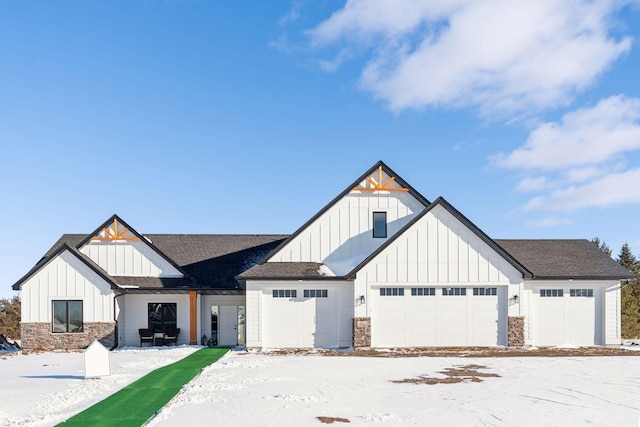 modern farmhouse with stone siding, board and batten siding, an attached garage, and roof with shingles