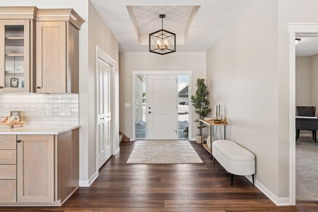 foyer entrance featuring dark wood-type flooring, an inviting chandelier, a raised ceiling, and baseboards