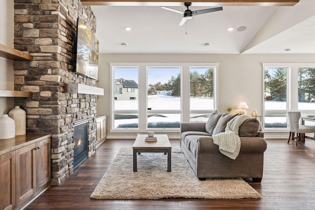 living area featuring lofted ceiling with beams, a stone fireplace, dark wood-style flooring, and a wealth of natural light