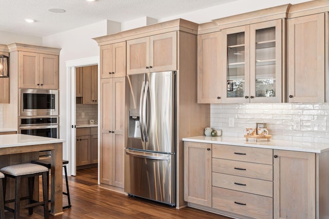 kitchen featuring stainless steel appliances, light brown cabinetry, light countertops, and glass insert cabinets