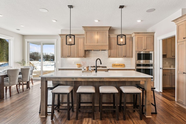 kitchen featuring a center island with sink, appliances with stainless steel finishes, a kitchen breakfast bar, dark wood-style flooring, and light countertops