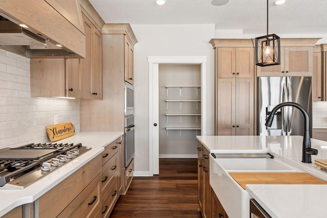 kitchen with dark wood-style floors, hanging light fixtures, decorative backsplash, appliances with stainless steel finishes, and wall chimney exhaust hood