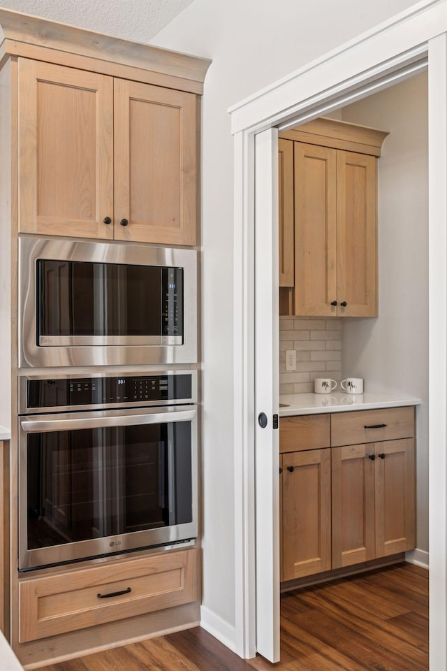 kitchen with stainless steel appliances, dark wood finished floors, backsplash, and light brown cabinetry