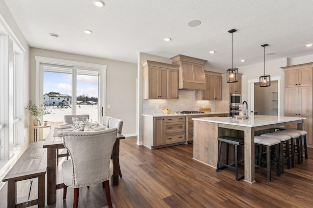 kitchen with light countertops, dark wood-style flooring, premium range hood, and a kitchen breakfast bar