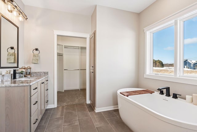 full bathroom with a freestanding bath, a spacious closet, vanity, tile patterned flooring, and baseboards