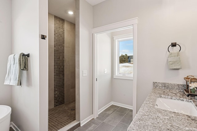 bathroom with tiled shower, vanity, baseboards, and tile patterned floors