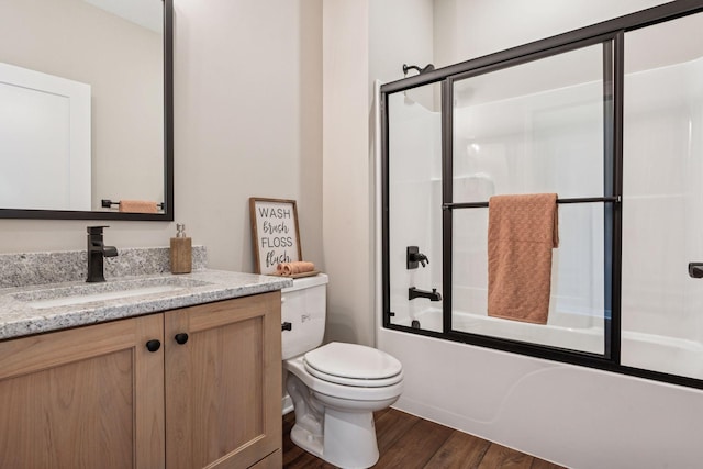 bathroom featuring toilet, bath / shower combo with glass door, wood finished floors, and vanity