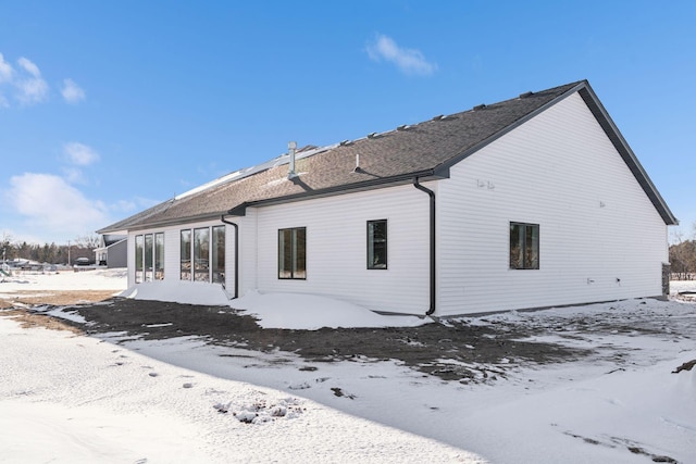 snow covered rear of property with a shingled roof