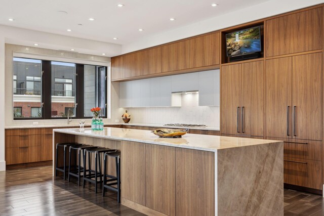 kitchen with a kitchen breakfast bar, a spacious island, tasteful backsplash, light stone countertops, and dark hardwood / wood-style flooring