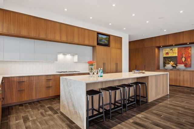 kitchen featuring decorative backsplash, a breakfast bar area, dark hardwood / wood-style floors, and a large island with sink