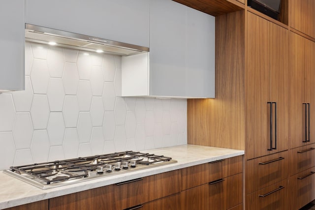 kitchen featuring tasteful backsplash, light stone counters, ventilation hood, and stainless steel gas cooktop