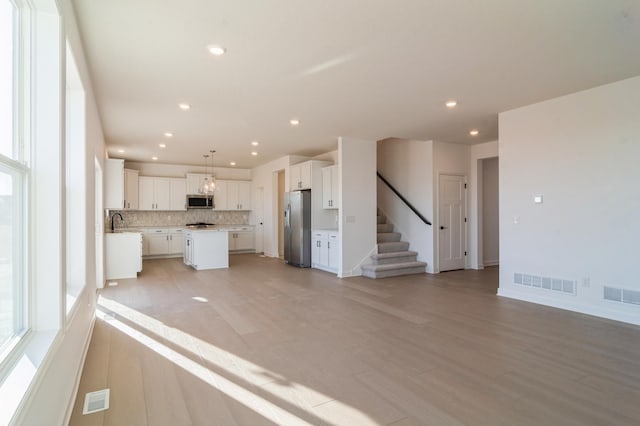 kitchen featuring stainless steel appliances, a center island, tasteful backsplash, white cabinets, and decorative light fixtures