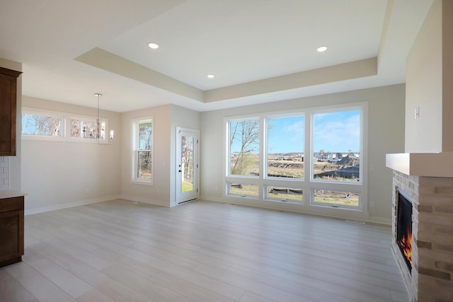 13104 Ghia Ct NE, Blaine, MN 55449 - unfurnished living room featuring a chandelier, light wood-type flooring, a raised ceiling, a lit fireplace, and baseboards