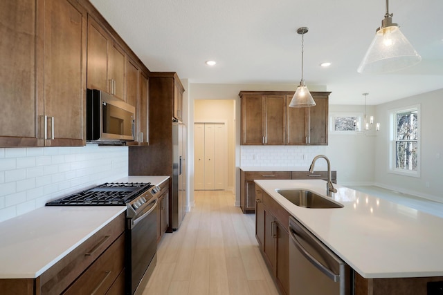 13104 Ghia Ct NE, Blaine, MN 55449 - kitchen featuring appliances with stainless steel finishes, a sink, an island with sink, backsplash, and hanging light fixtures