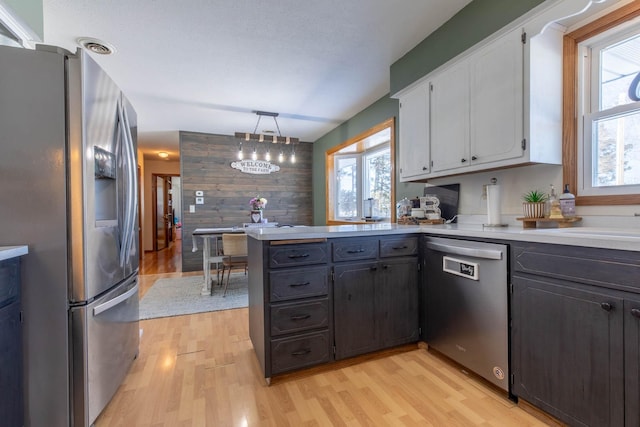 kitchen featuring light wood-style floors, appliances with stainless steel finishes, light countertops, white cabinets, and a peninsula