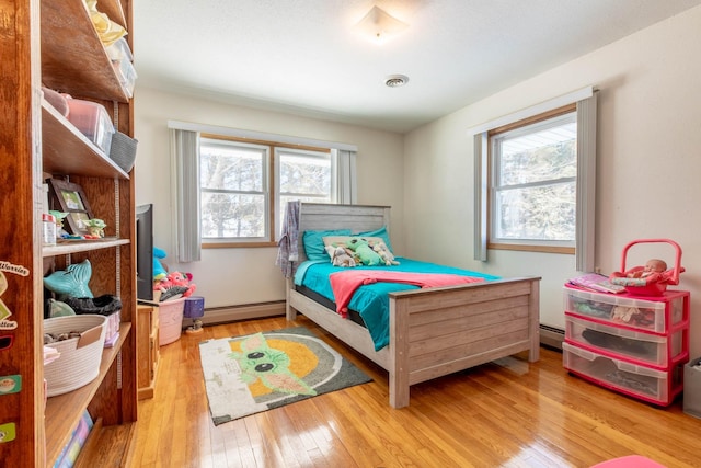 bedroom with a baseboard radiator, visible vents, hardwood / wood-style flooring, and multiple windows