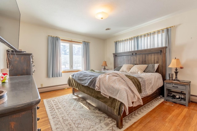 bedroom featuring baseboard heating, light wood-style flooring, and baseboards