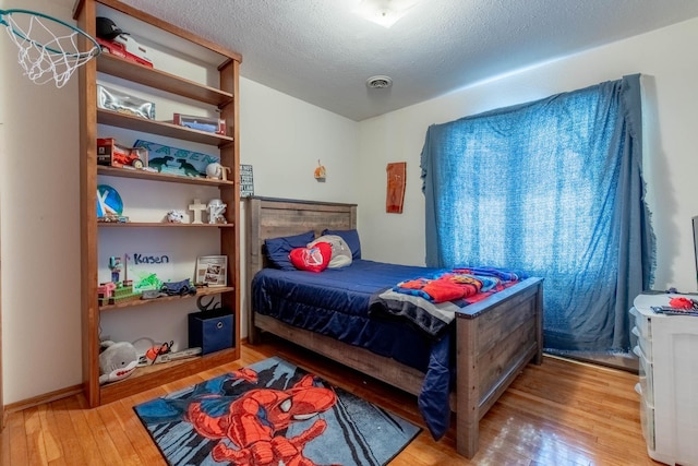 bedroom with a textured ceiling, hardwood / wood-style floors, and visible vents