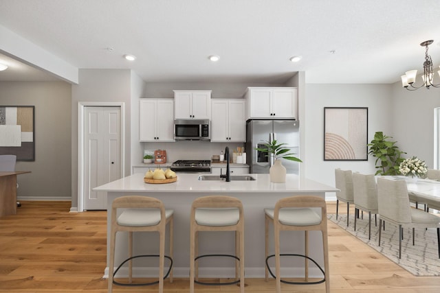 kitchen with a kitchen island with sink, a sink, stainless steel appliances, light countertops, and light wood-style floors