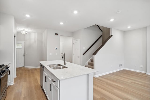 kitchen featuring a sink, range with gas cooktop, light wood-style floors, light stone countertops, and dishwasher