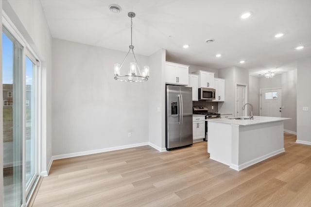 kitchen featuring light wood finished floors, a chandelier, decorative backsplash, appliances with stainless steel finishes, and a sink