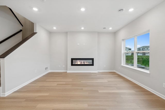 unfurnished living room featuring light wood-type flooring, visible vents, a glass covered fireplace, recessed lighting, and baseboards