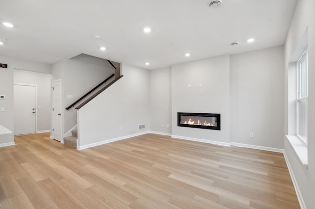 unfurnished living room featuring baseboards, stairway, recessed lighting, light wood-style flooring, and a glass covered fireplace