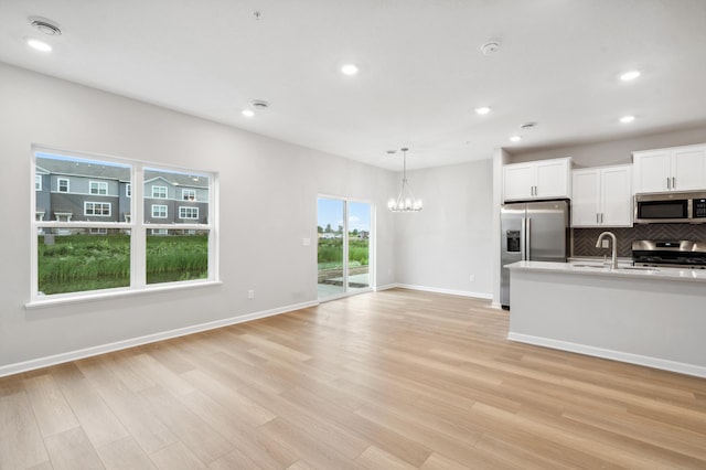 kitchen with backsplash, light wood-style flooring, appliances with stainless steel finishes, white cabinetry, and a sink