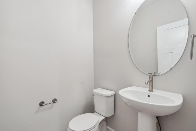 half bathroom featuring toilet, baseboards, and a sink