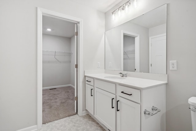 bathroom featuring toilet, vanity, a walk in closet, and baseboards