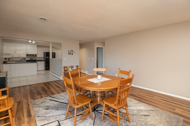 dining room featuring a baseboard radiator, light hardwood / wood-style floors, and a textured ceiling