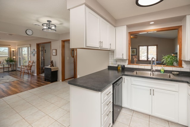 kitchen featuring sink, backsplash, white cabinetry, light tile patterned floors, and black dishwasher