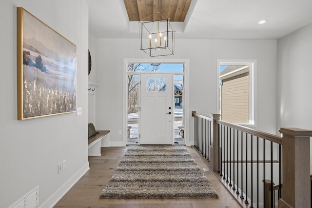 entrance foyer with hardwood / wood-style flooring, wooden ceiling, a tray ceiling, and a notable chandelier