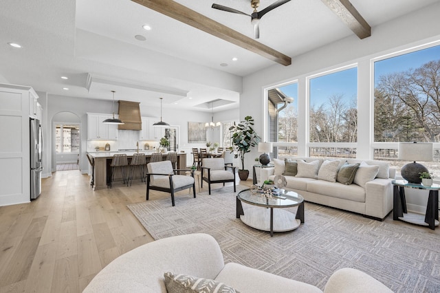 living room with ceiling fan with notable chandelier, beam ceiling, and light wood-type flooring