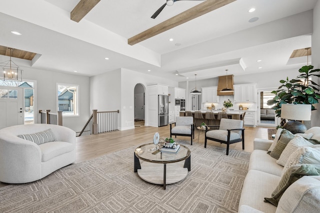 living room featuring beam ceiling, sink, ceiling fan with notable chandelier, and light hardwood / wood-style floors