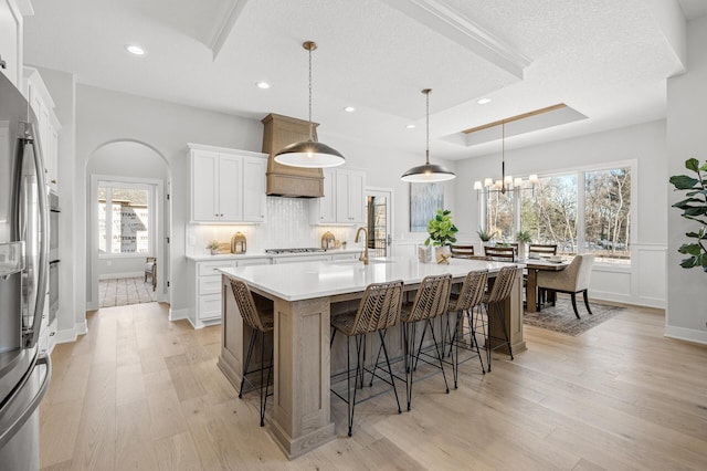 kitchen featuring pendant lighting, a large island with sink, white cabinets, light wood-type flooring, and a breakfast bar