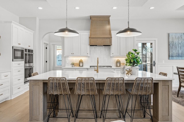 kitchen with a large island with sink, custom exhaust hood, decorative light fixtures, white cabinetry, and a breakfast bar