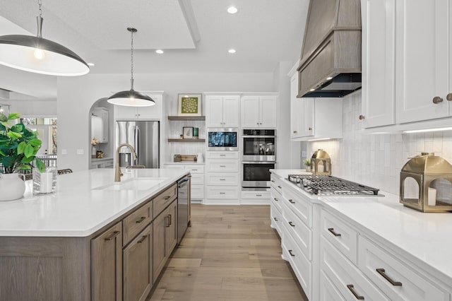 kitchen featuring custom exhaust hood, decorative light fixtures, an island with sink, and white cabinetry