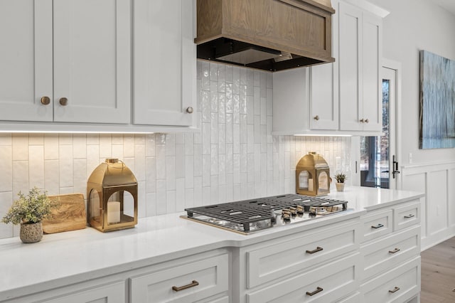 kitchen with decorative backsplash, white cabinets, stainless steel gas stovetop, and custom range hood