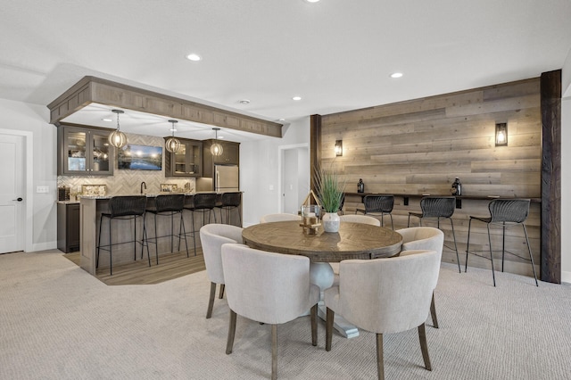 dining area with wood walls, light colored carpet, and indoor bar