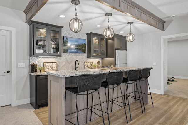 kitchen featuring light stone countertops, pendant lighting, a kitchen island with sink, and stainless steel refrigerator