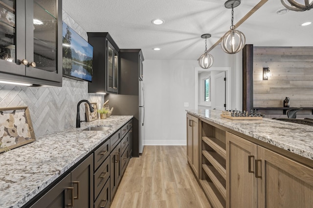 kitchen with tasteful backsplash, light hardwood / wood-style floors, sink, light stone countertops, and a textured ceiling