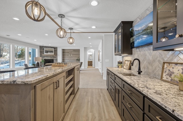 kitchen featuring a stone fireplace, tasteful backsplash, light stone counters, and sink