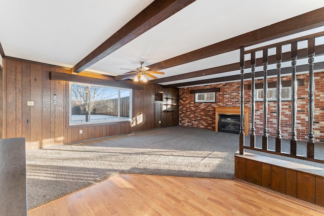 unfurnished living room with ceiling fan, hardwood / wood-style floors, beam ceiling, a fireplace, and wood walls