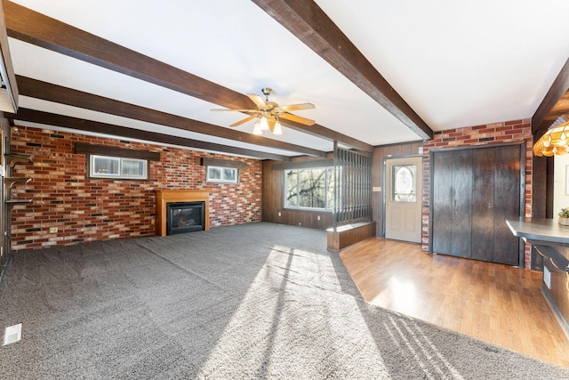 unfurnished living room featuring wood-type flooring, brick wall, ceiling fan, and beam ceiling